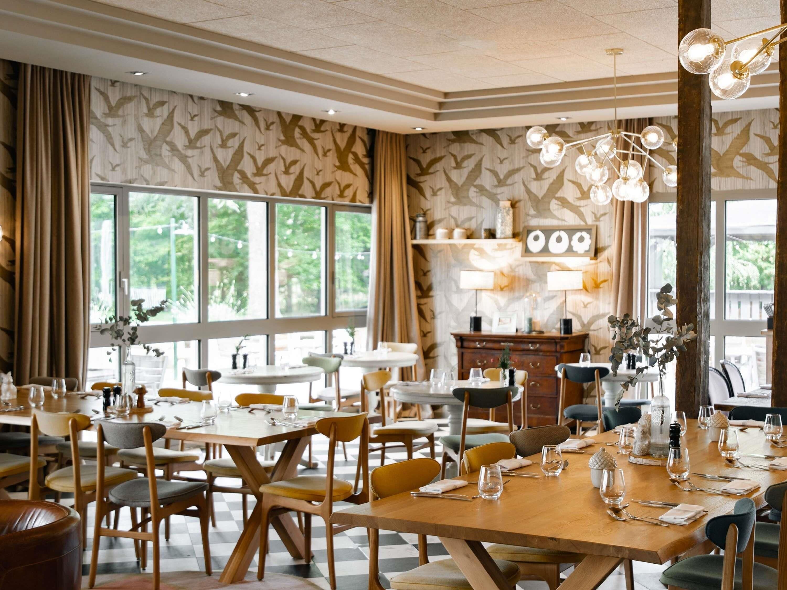 A dining area with multiple tables and chairs, large windows, and a decorative ceiling light fixture.