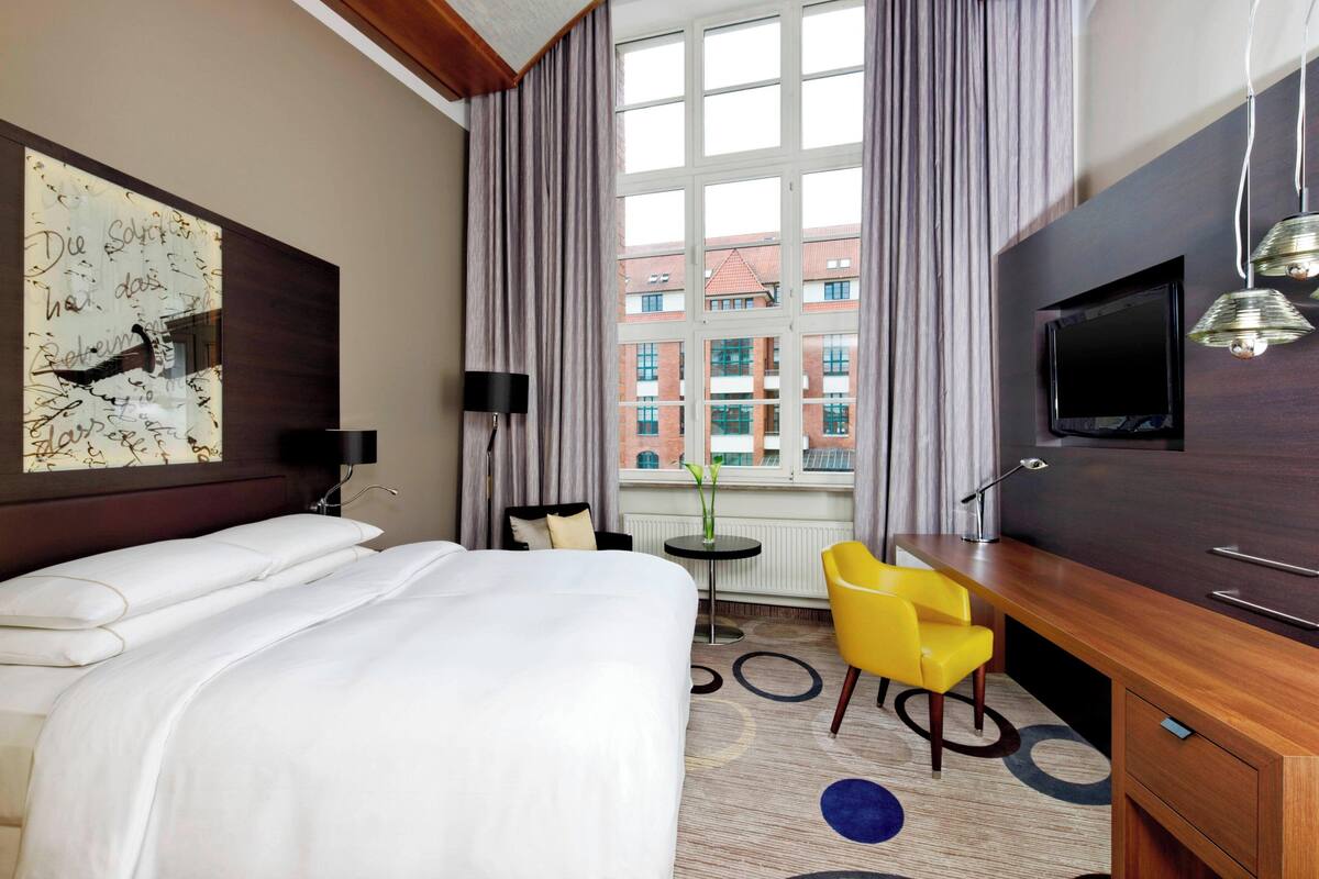 A hotel room with a large bed, a desk with a chair, a TV, and a window with curtains.