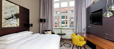 Una habitación de hotel con una cama grande, un escritorio con silla, un televisor y una ventana con cortinas.