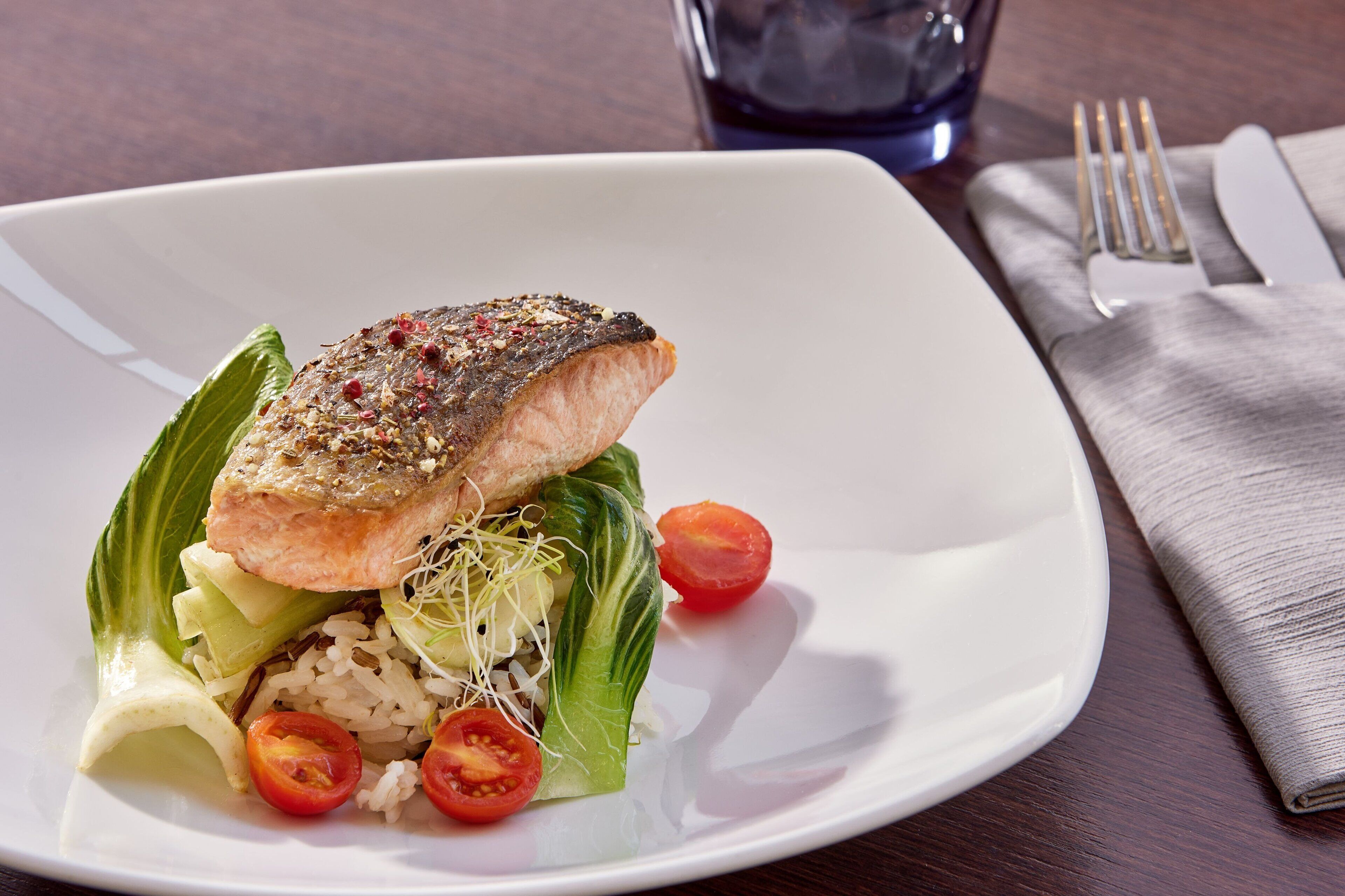 A white plate with a piece of salmon, rice, and vegetables.