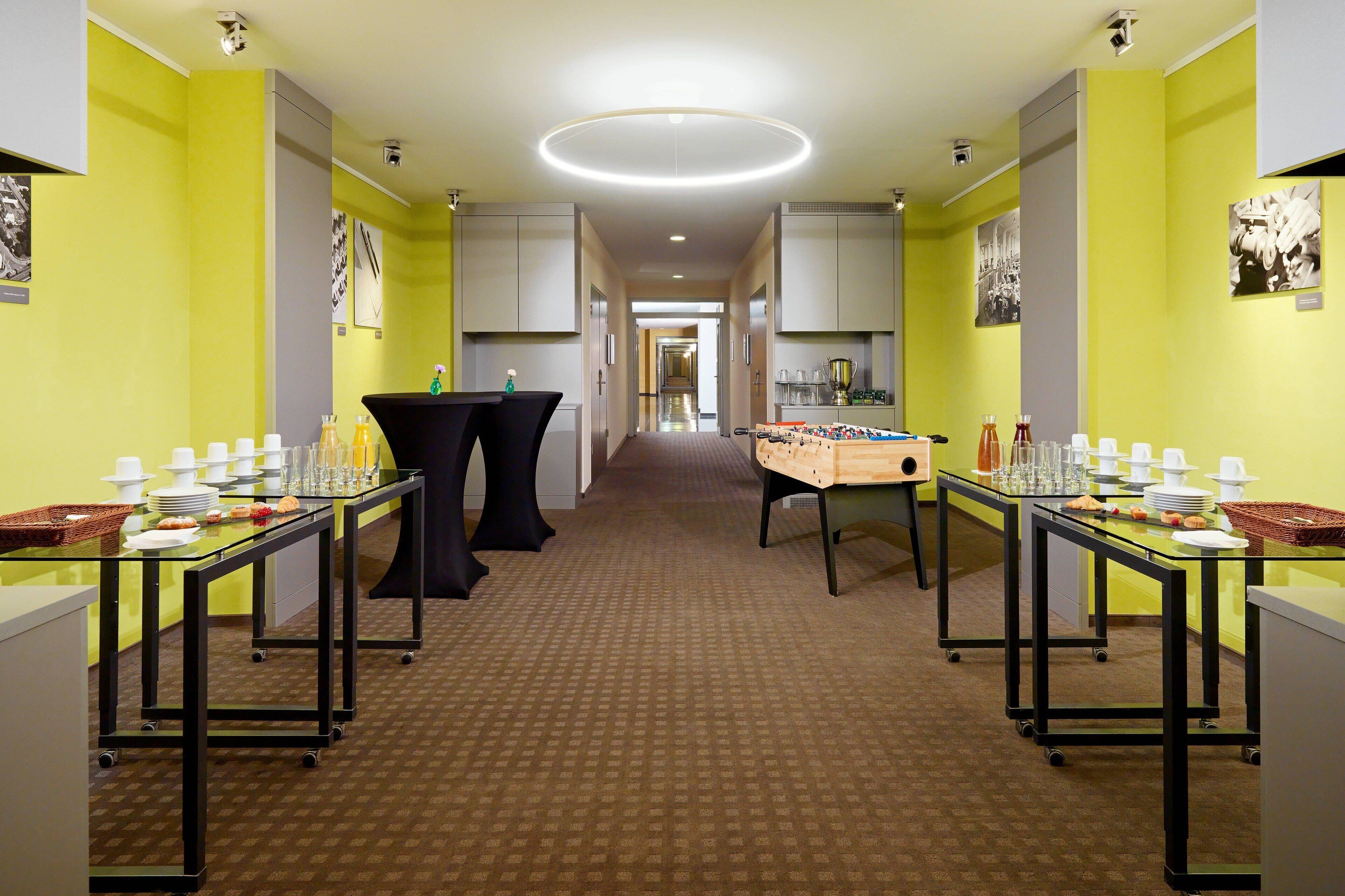 A hotel lobby with a central corridor, tables with dining ware, and a foosball table.