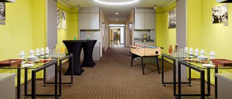 A hotel lobby with a central corridor, tables with dining ware, and a foosball table.