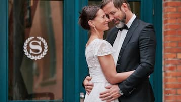 Una pareja se abraza frente a un edificio con una puerta con un monograma.