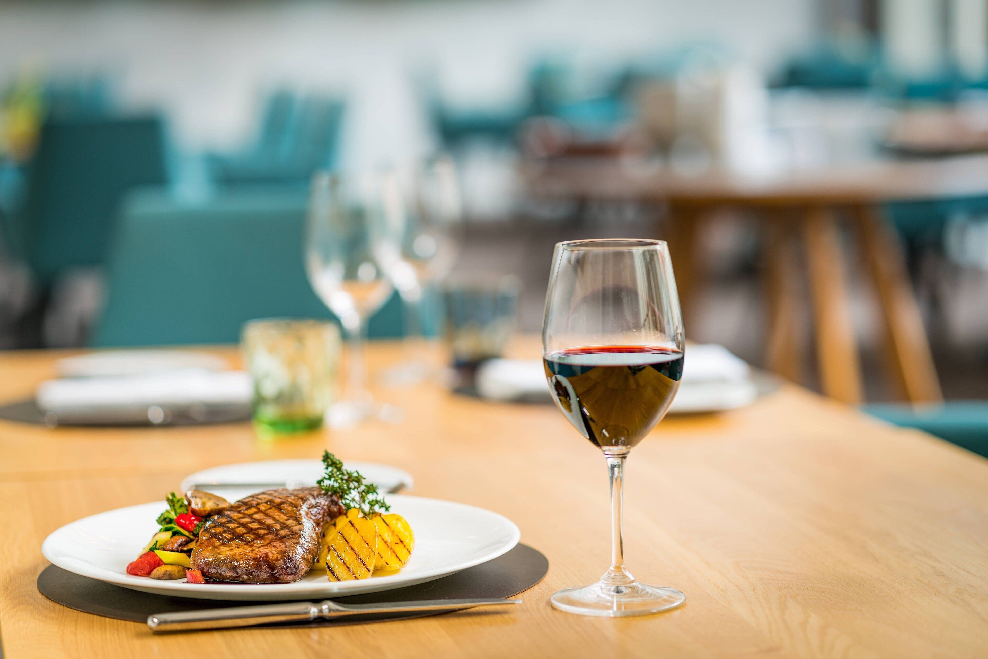 Une table à manger avec une assiette de steak grillé et de légumes, un verre de vin rouge et une fourchette.