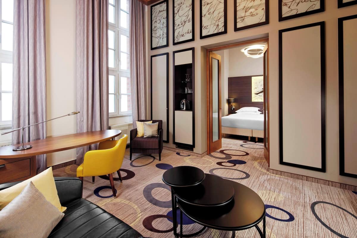 A hotel room with a desk, a yellow chair, a black sofa, and a bed.