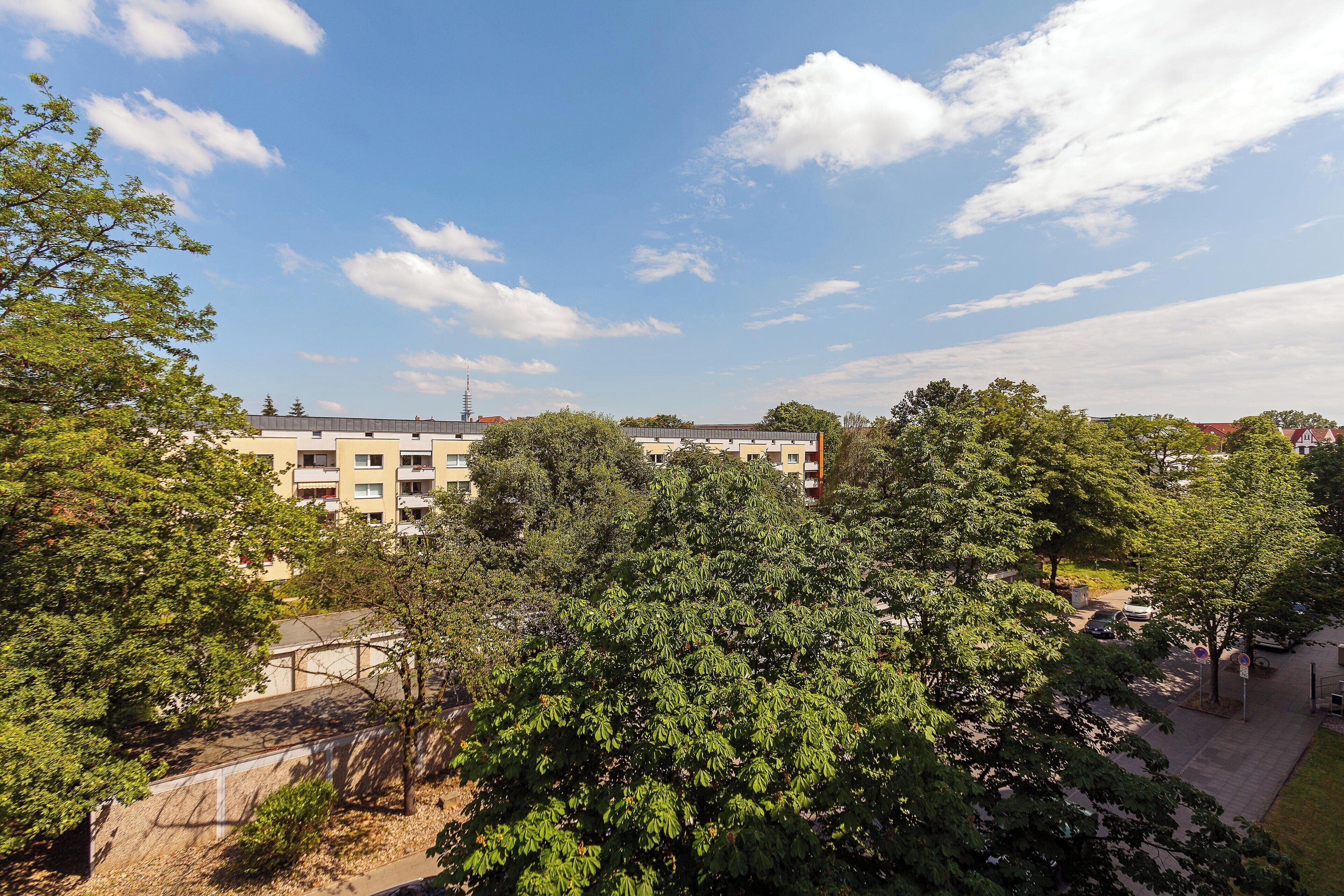 A multi-story building with a flat roof, surrounded by trees and a clear sky.