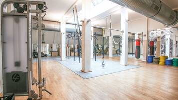Ein geräumiger Fitnessraum mit unterschiedlichen Trainingsgeräten, großen Fenstern und einer hohen Decke.