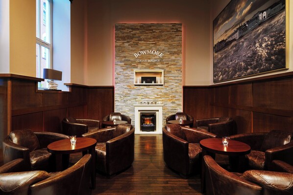 A Bowmore Cigar Lounge with leather seating, a fireplace, and a large framed picture on the wall.