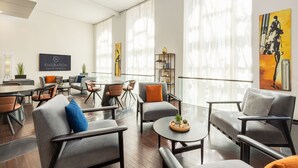 A modern hotel lobby with a mix of seating options, including sofas and chairs, a coffee table, and a dining area with a table and chairs.