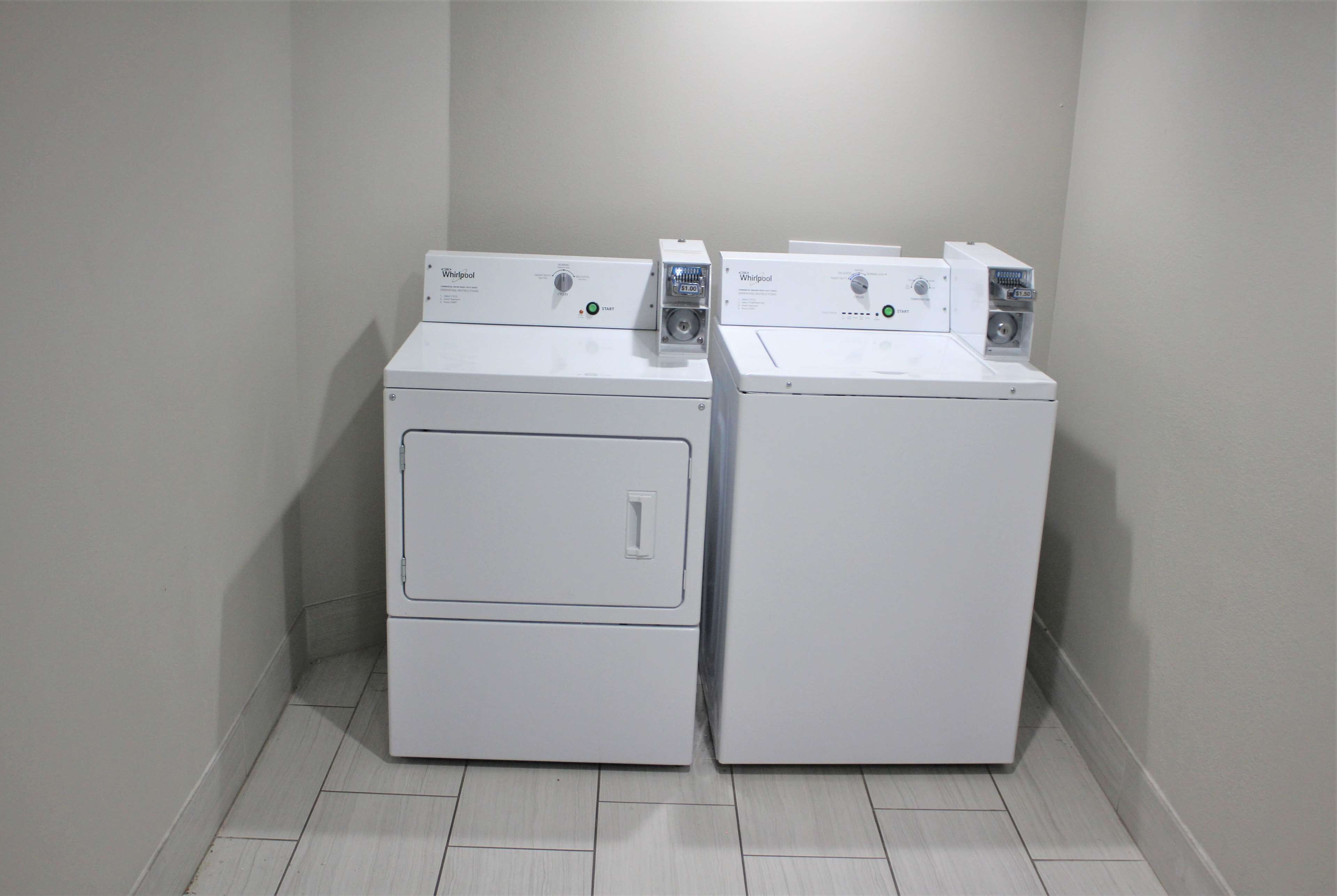 Duas máquinas de lavar Whirlpool brancas de abertura frontal num canto, com chão em azulejo.