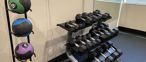 A gym with exercise equipment including a rack of dumbbells and a set of medicine balls.