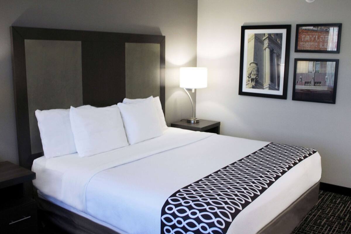 A hotel room with a large bed, a nightstand with a lamp, and framed pictures on the wall.