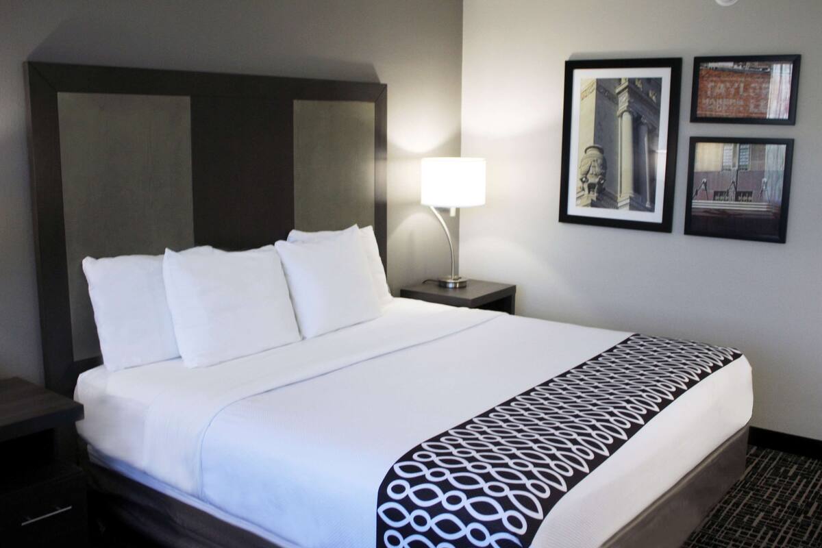 A hotel room with a large bed, a bedside table with a lamp, and framed pictures on the wall.