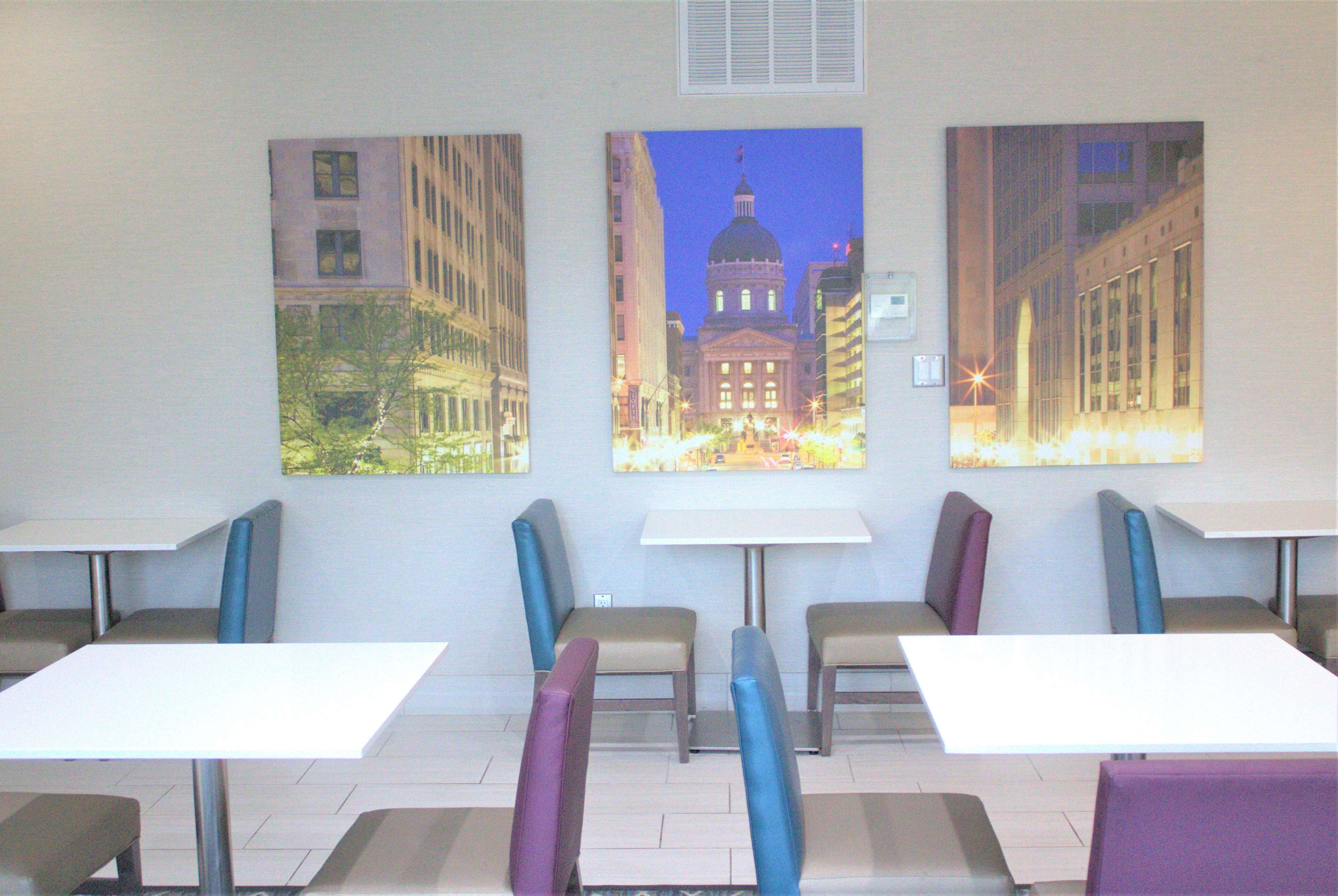 A dining area with tables and chairs, a large window with a view of a cityscape, and a wall-mounted air conditioning unit.