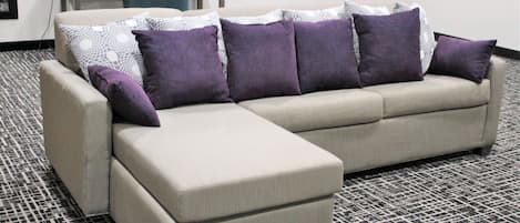 Un sofá seccional color beige con una chaise, acompañado de un tapete estampado y un escritorio con una silla al fondo.