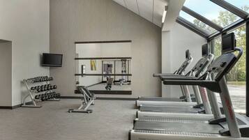 Une salle de sport équipée de tapis de course, d’haltères et d’un miroir.