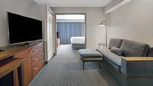 A hotel room with a flat-screen TV on a wooden dresser, a grey sofa with a wooden coffee table, a small side table, and a bed with a blue curtain. - Courtyard Chicago Elmhurst/Oakbrook Area (Elmhurst)