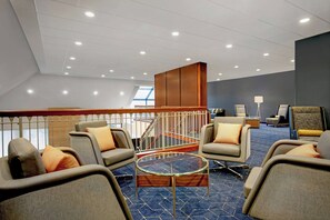 A hotel lobby with a blue carpet, multiple seating areas with cushioned chairs, a glass coffee table, and a staircase with a railing. - Courtyard Chicago Elmhurst/Oakbrook Area (Elmhurst)
