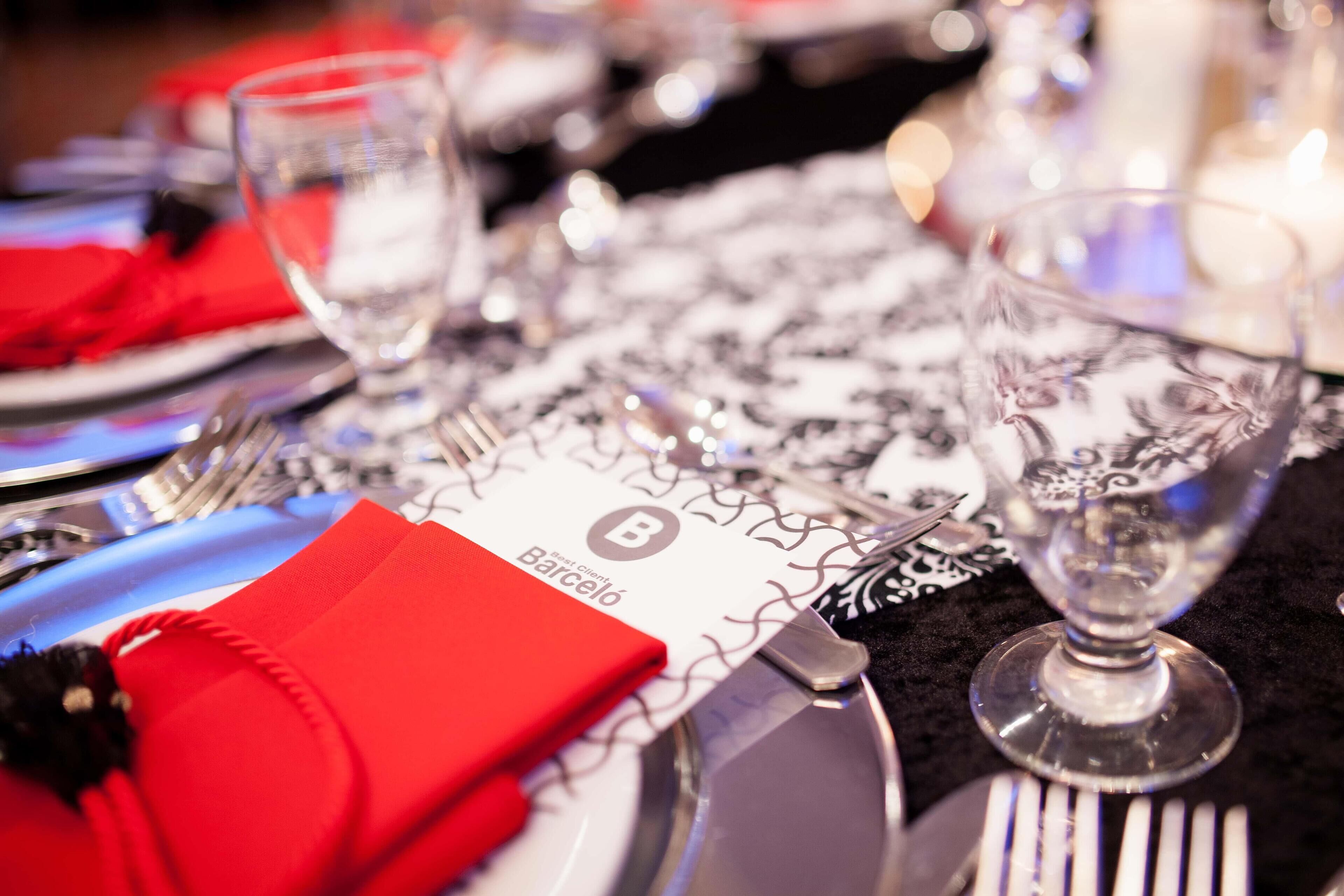Une table dressée avec une serviette rouge, un verre à vin et une assiette ornée d’un logo.