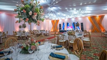 A banquet hall with round tables set for a formal event, featuring floral centerpieces and gold-rimmed glassware.