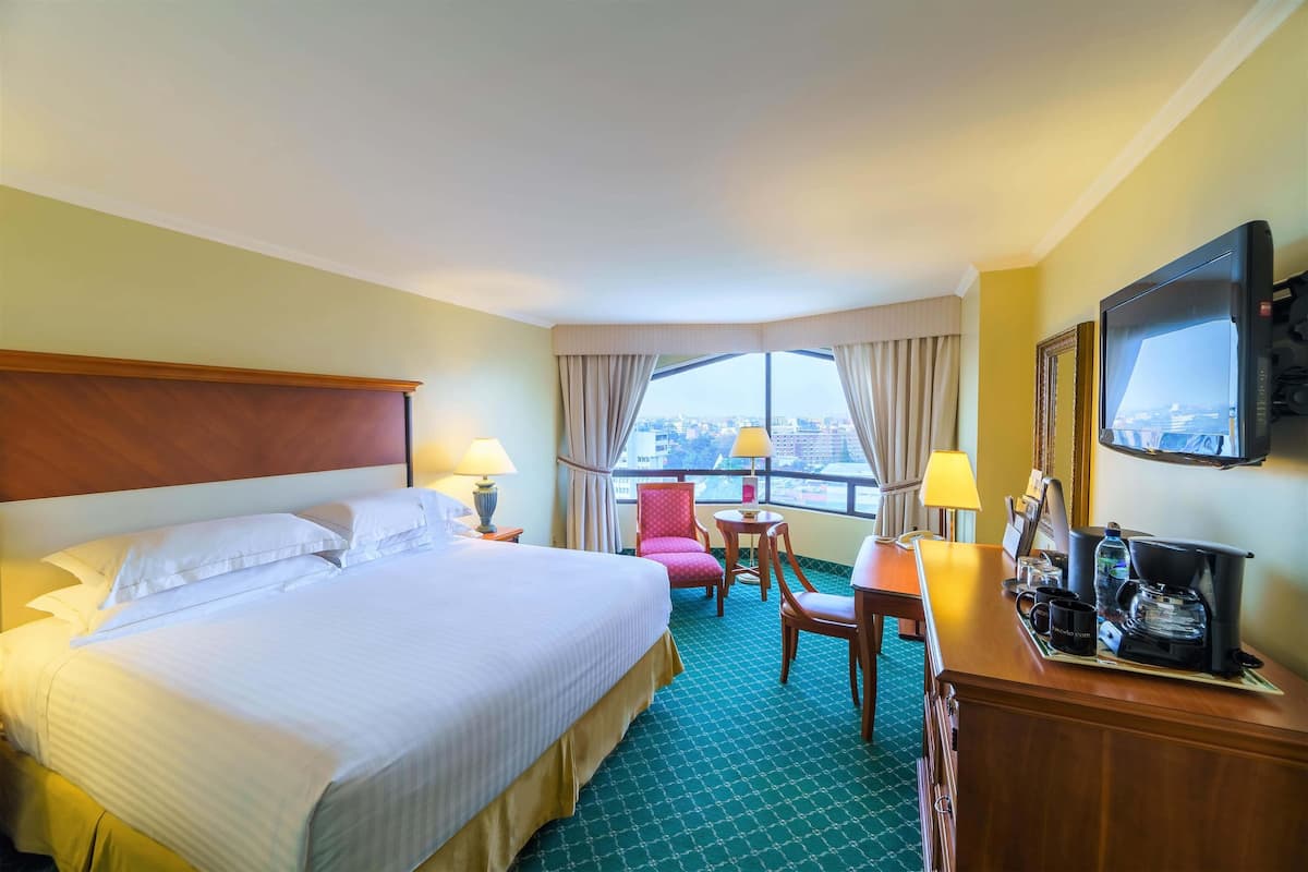 Une chambre d’hôtel avec un grand lit, un bureau avec une machine à café, une chaise et un téléviseur.