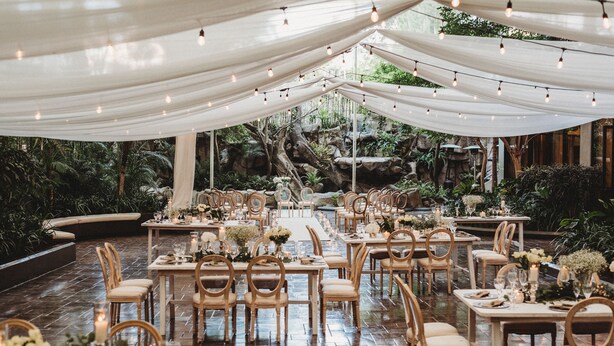An indoor venue with tables and chairs arranged for dining, surrounded by draped fabric and string lights. - Barceló Guatemala City (Guatemala City)