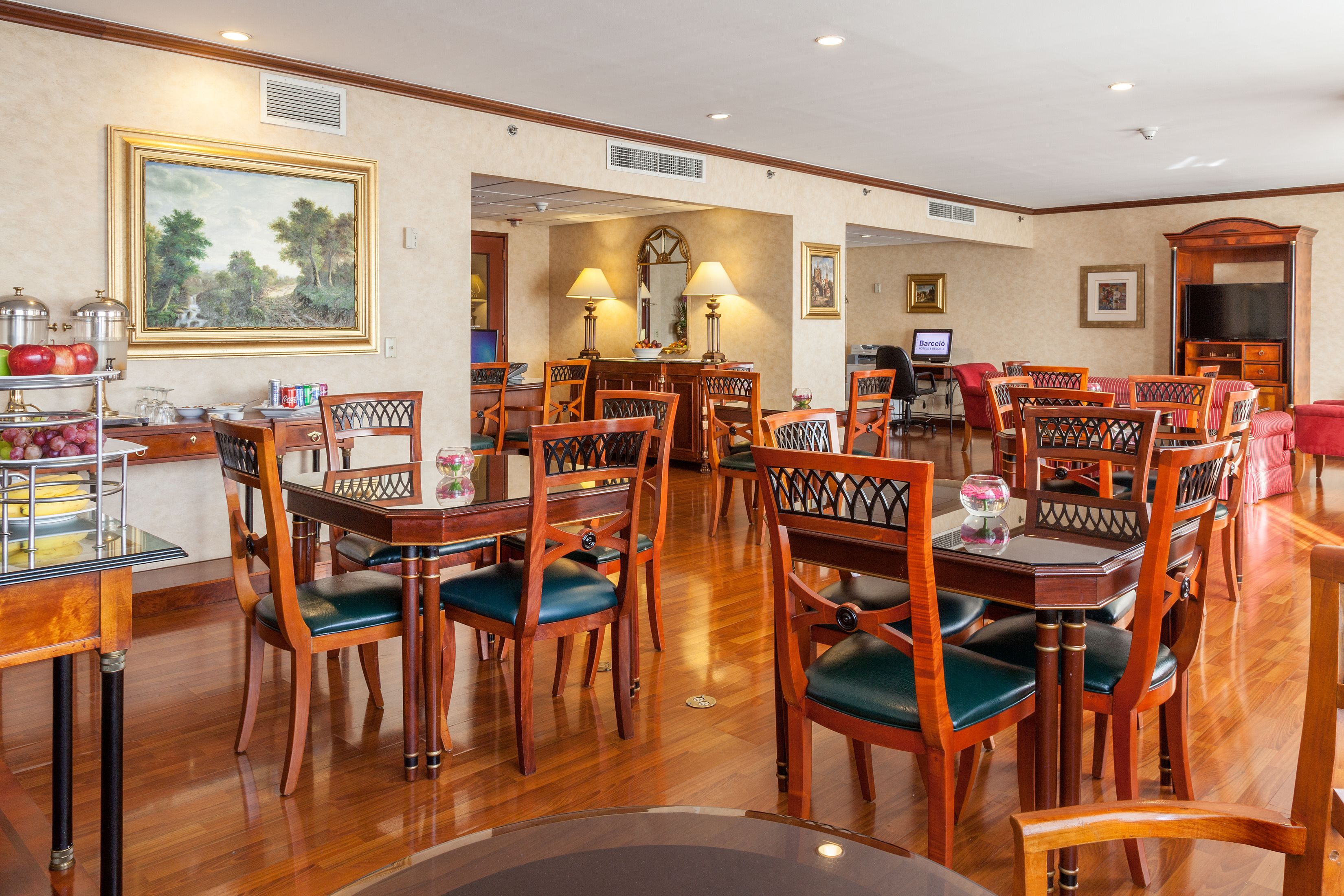 A spacious dining area with wooden tables and chairs, a large painting on the wall, and a television in the background.