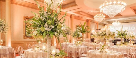 Un salón de banquetes con mesas redondas, sillas transparentes y centros de mesa florales.