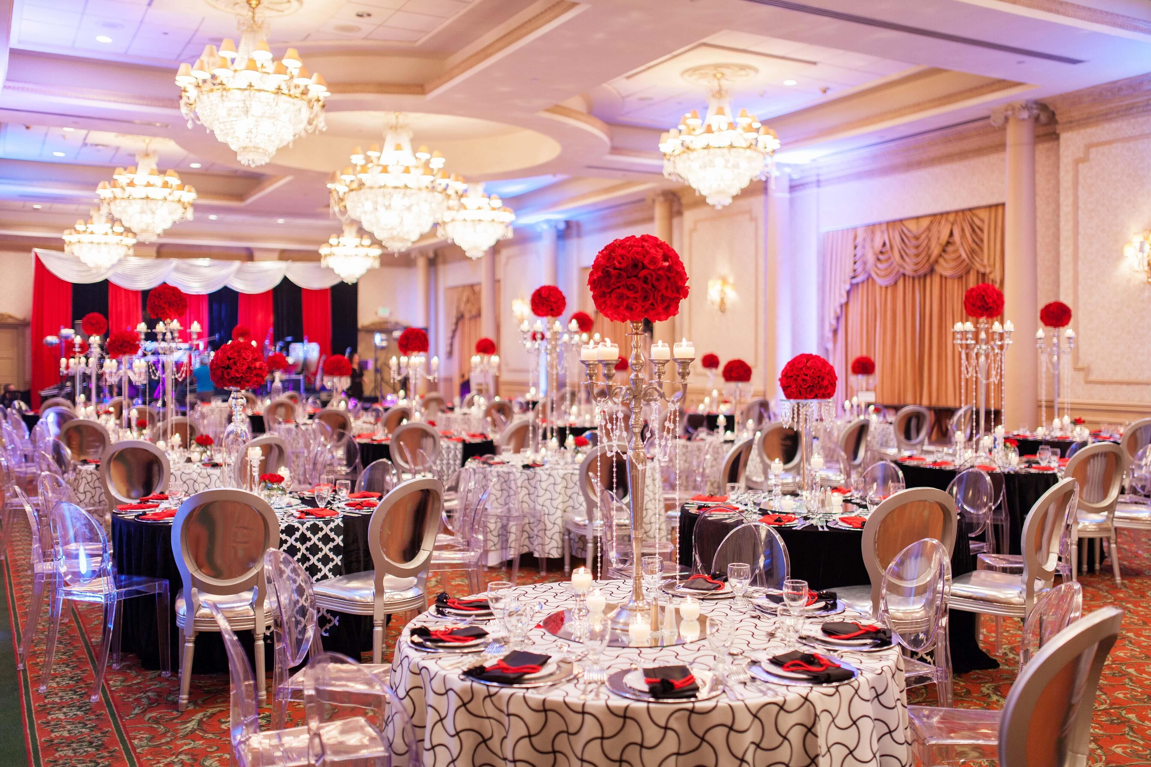 A banquet hall with round tables, clear chairs, and chandeliers.