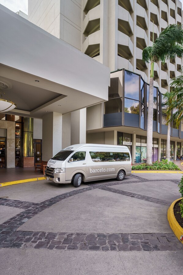 A white van parked in front of a modern building with a large entrance and a visible sign for 'United'. - Barceló Guatemala City (Guatemala City)