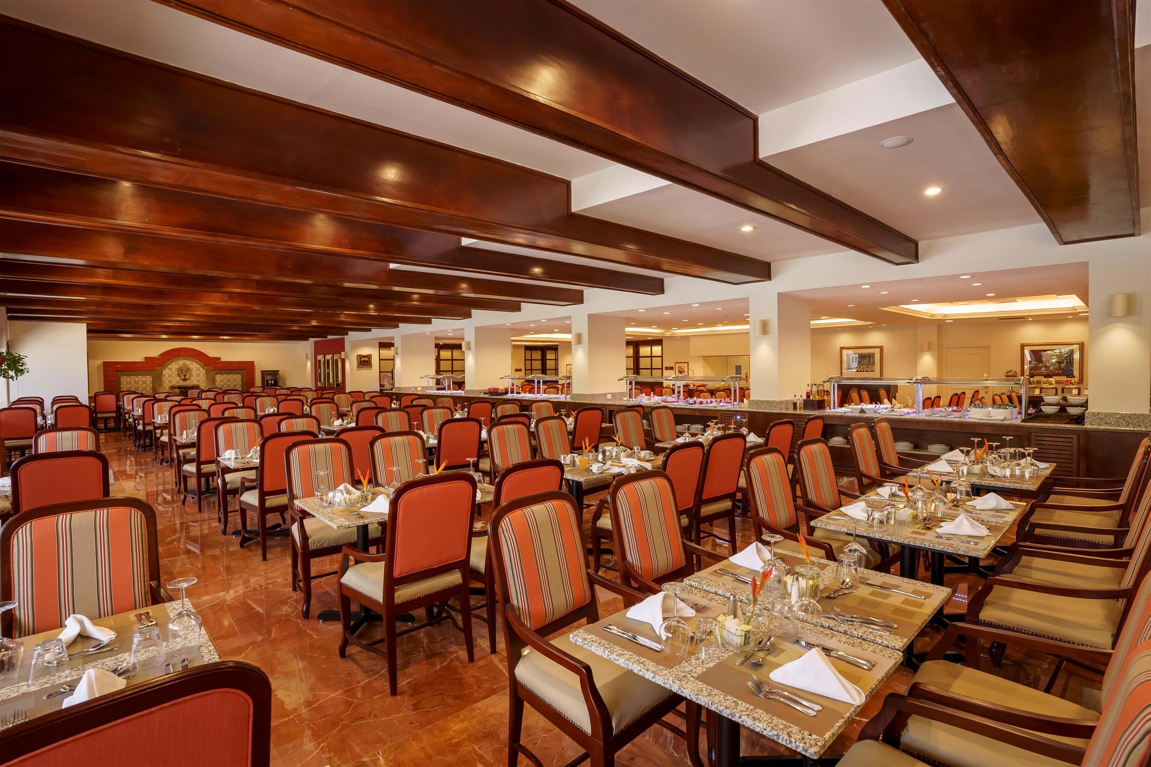 Un comedor amplio con varias mesas y sillas, un espacio tipo buffet y un techo alto con vigas de madera.
