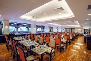 Un comedor amplio con varias mesas y sillas, piso de mármol pulido y un diseño de techo moderno.