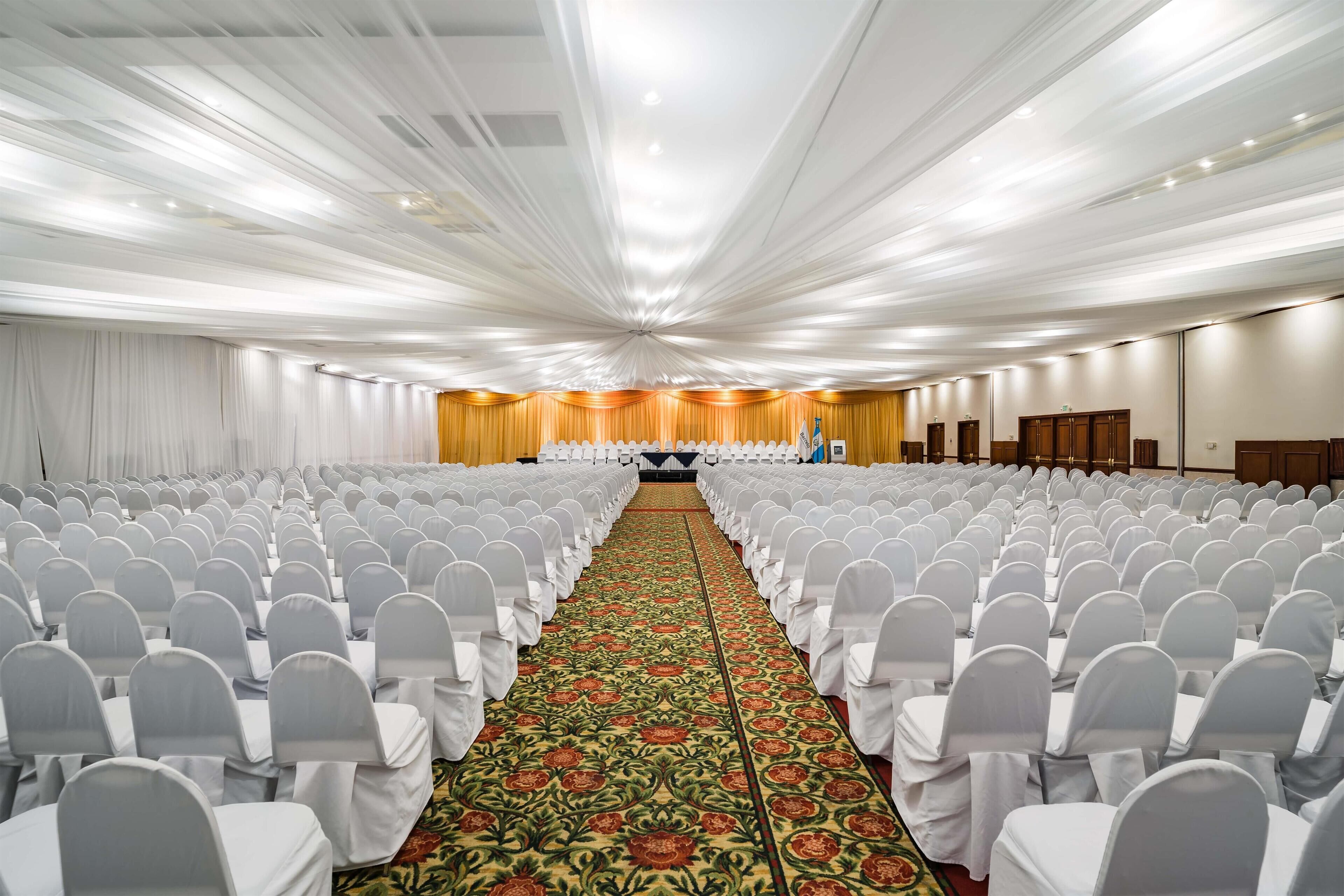 Une grande salle de conférence avec des rangées de chaises blanches et une allée recouverte de moquette.