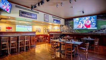 Un espace bar avec des meubles en bois, un grand écran diffusant des événements sportifs et des tableaux encadrés aux murs.