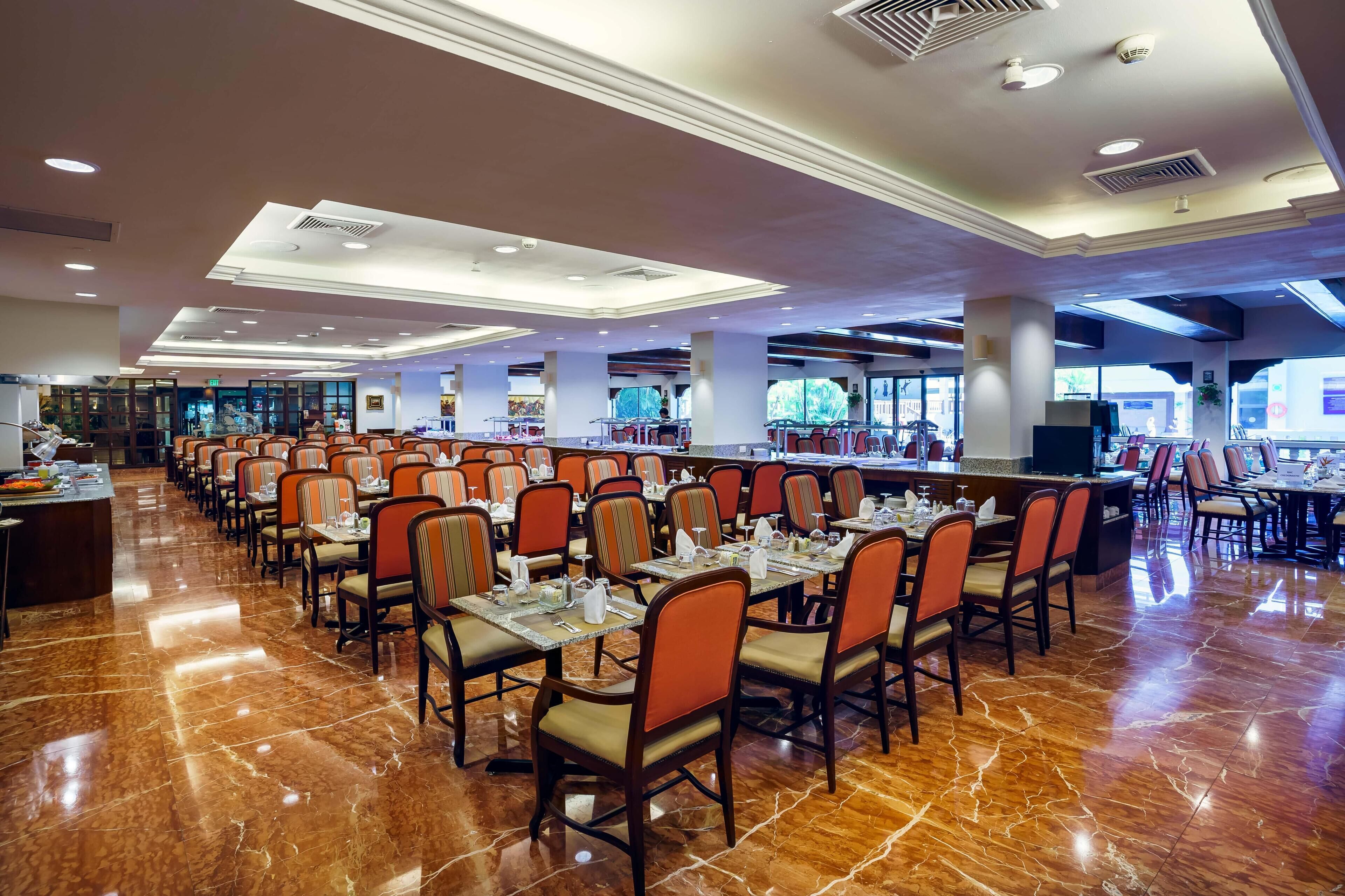 Uma sala de jantar espaçosa com várias mesas e cadeiras, piso de mármore polido e design de teto moderno.