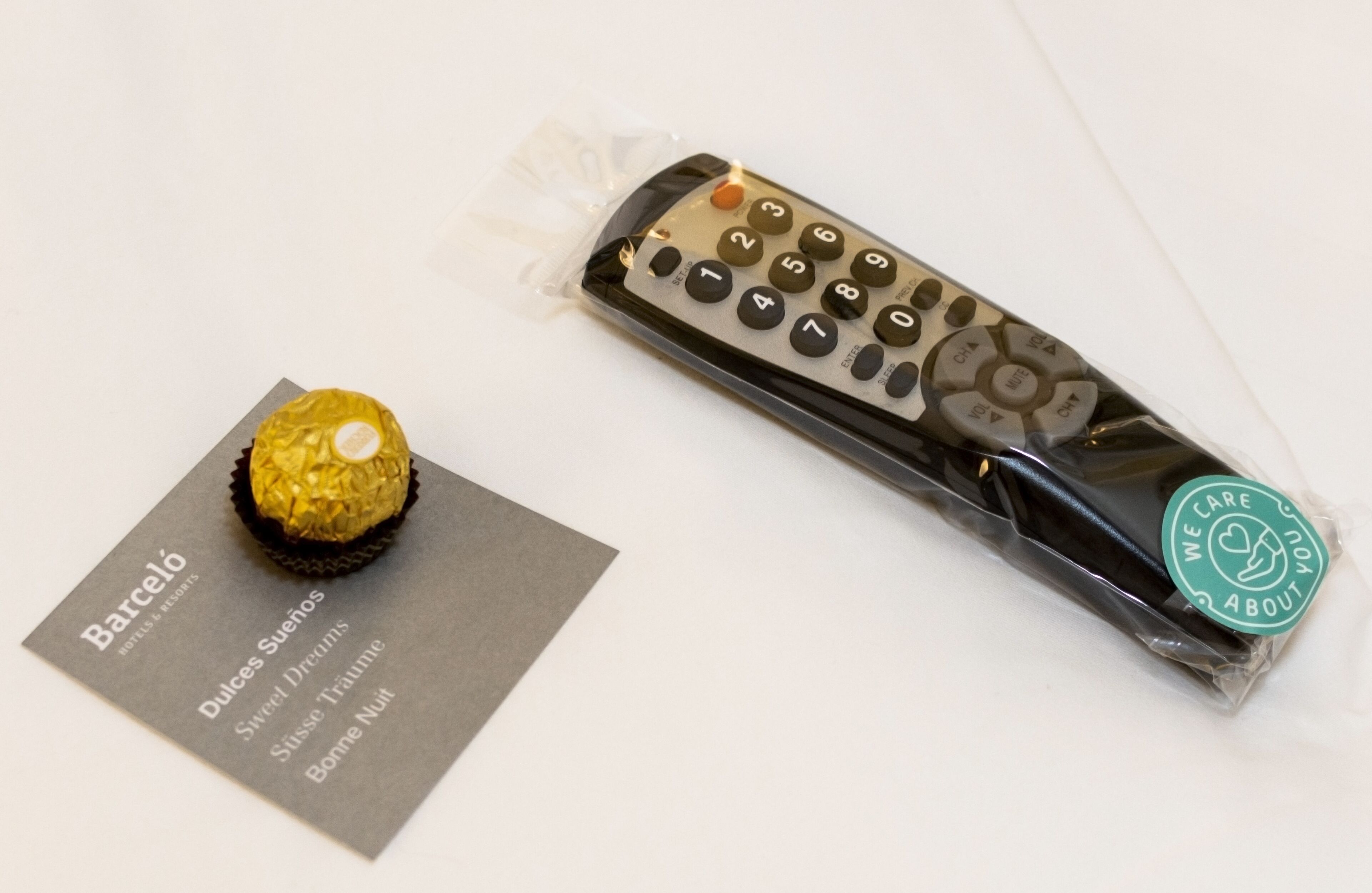 A chocolate bar, a remote control, and a business card with the text "Barceló Hotels & Resorts" and "Dulces Sueños."