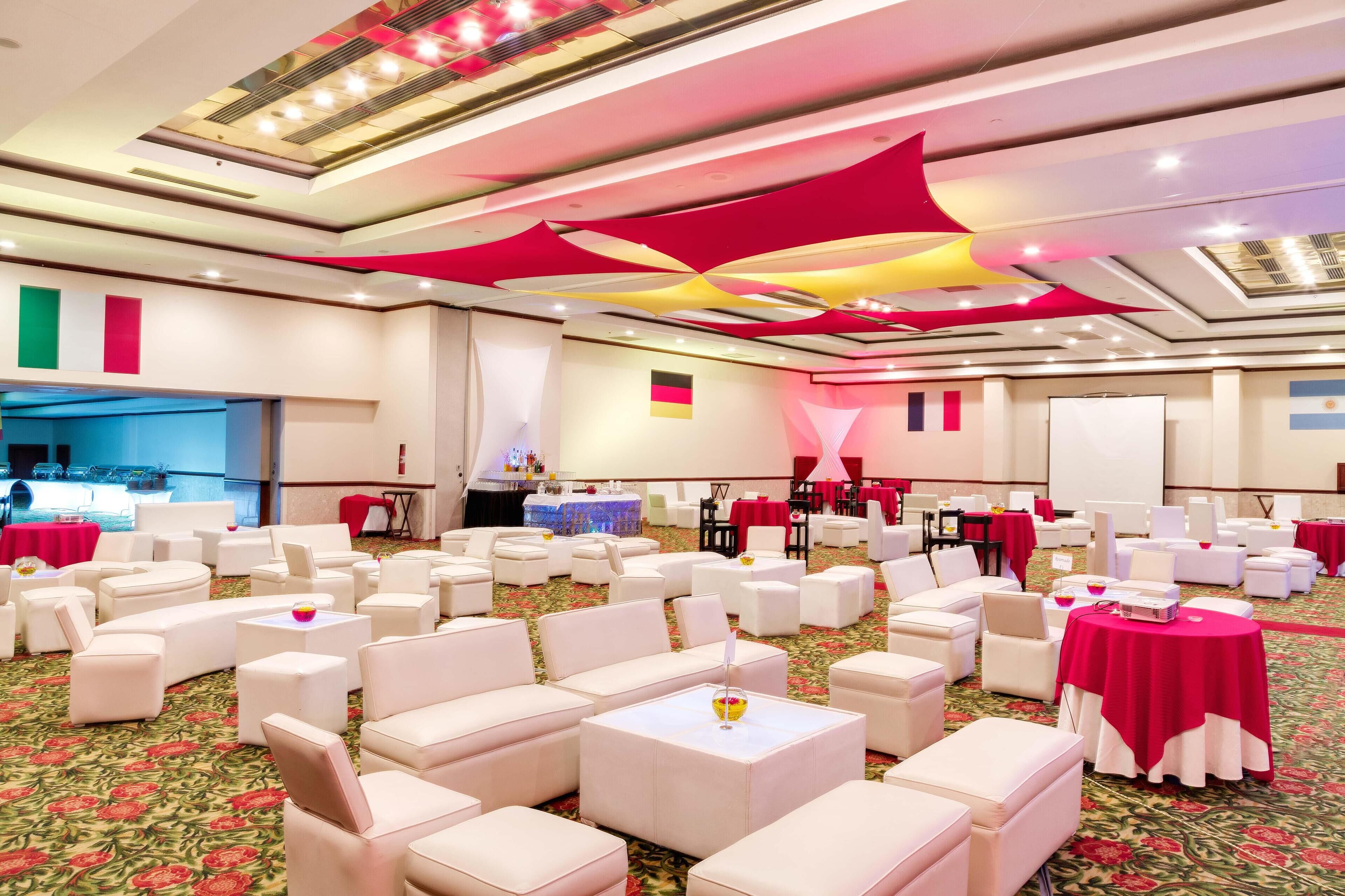 A banquet hall with white chairs and tables, red drapes, and a floral carpet.