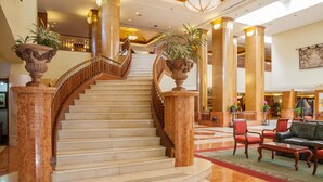 A grand staircase with marble steps and wooden railings, flanked by large columns and potted plants. - Barceló Guatemala City (Guatemala City)