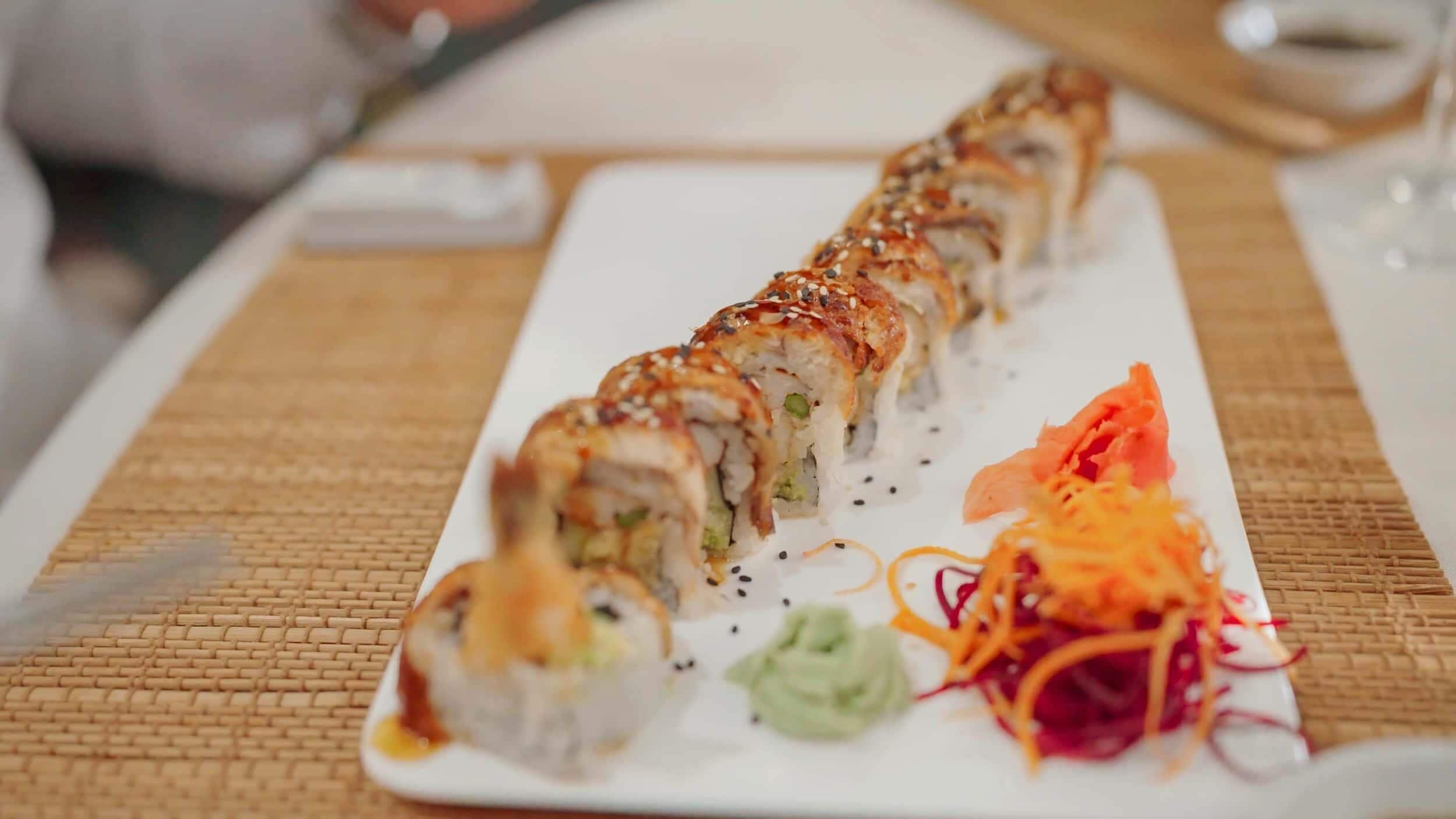 Een sushi schaal met diverse soorten rolletjes, een klein schaaltje wasabi, ingemaakte gember en een portie gesneden groenten.