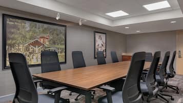 A conference room with a long table, black chairs, a large framed picture of a building, and a ceiling with recessed lighting.