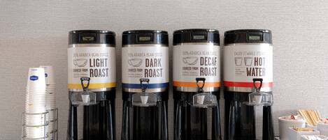 Quatre distributeurs de café, chacun portant une étiquette indiquant le type de torréfaction, et une pile de gobelets jetables.