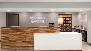 A reception desk with a 'Welcome to Hampton' sign, a Hilton Honors badge, and a snack display. - Hampton Inn Dubuque (Dubuque)