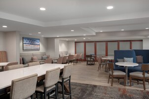 Un moderno vestíbulo de hotel con una larga mesa de comedor, varias sillas, un sofá azul y un cuadro grande en la pared.