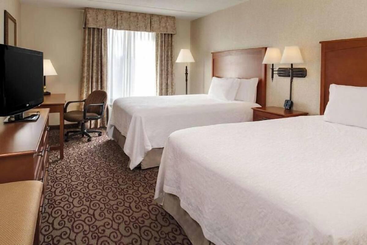 A hotel room with two beds, a television, a desk with a chair, and a patterned carpet.