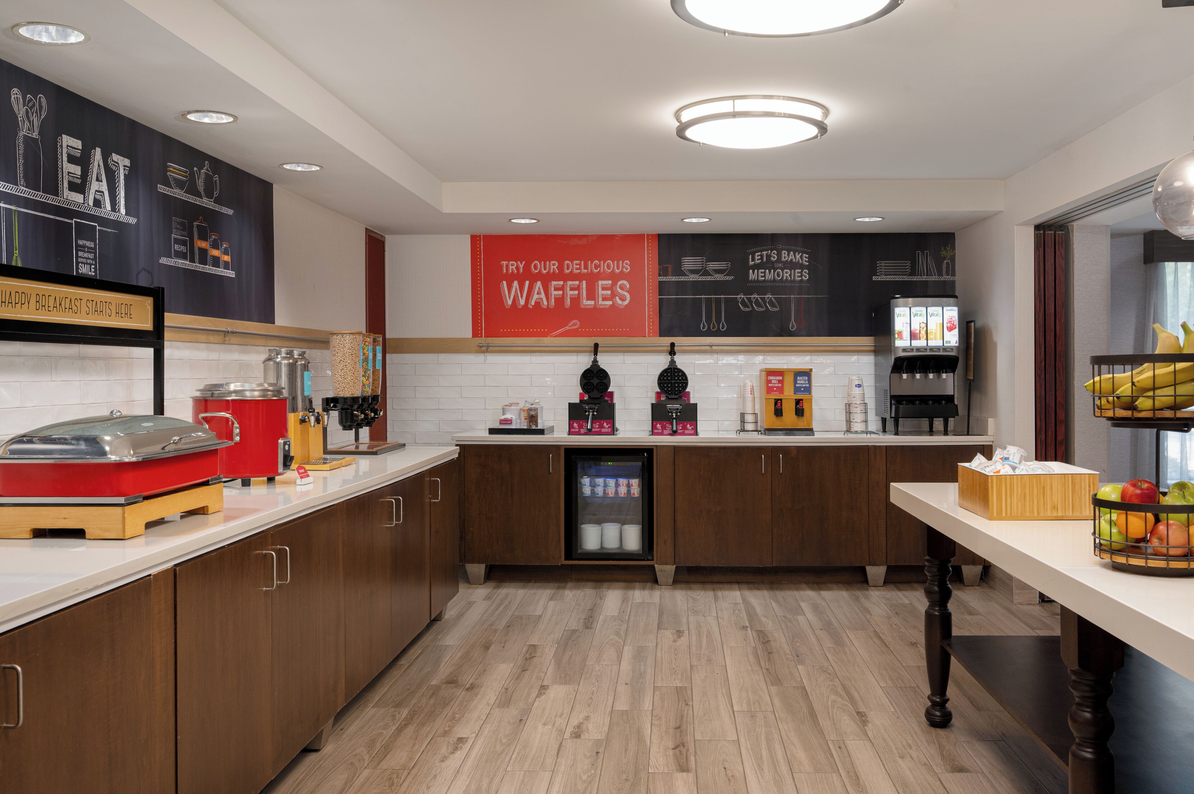 A modern kitchen with a waffle station, a coffee machine, and a refrigerator.