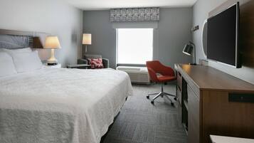 A hotel room with a large bed, a desk, a chair, a flat-screen TV, and a window with a view.