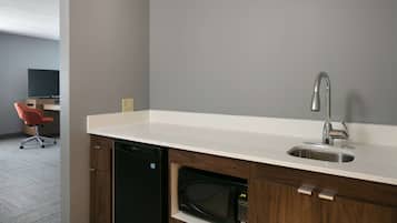 A modern kitchen with a white countertop, stainless steel sink, and built-in microwave.