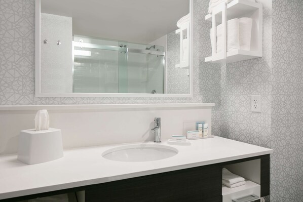 Une salle de bain avec un lavabo blanc, une douche à parois de verre et un miroir au-dessus du lavabo.