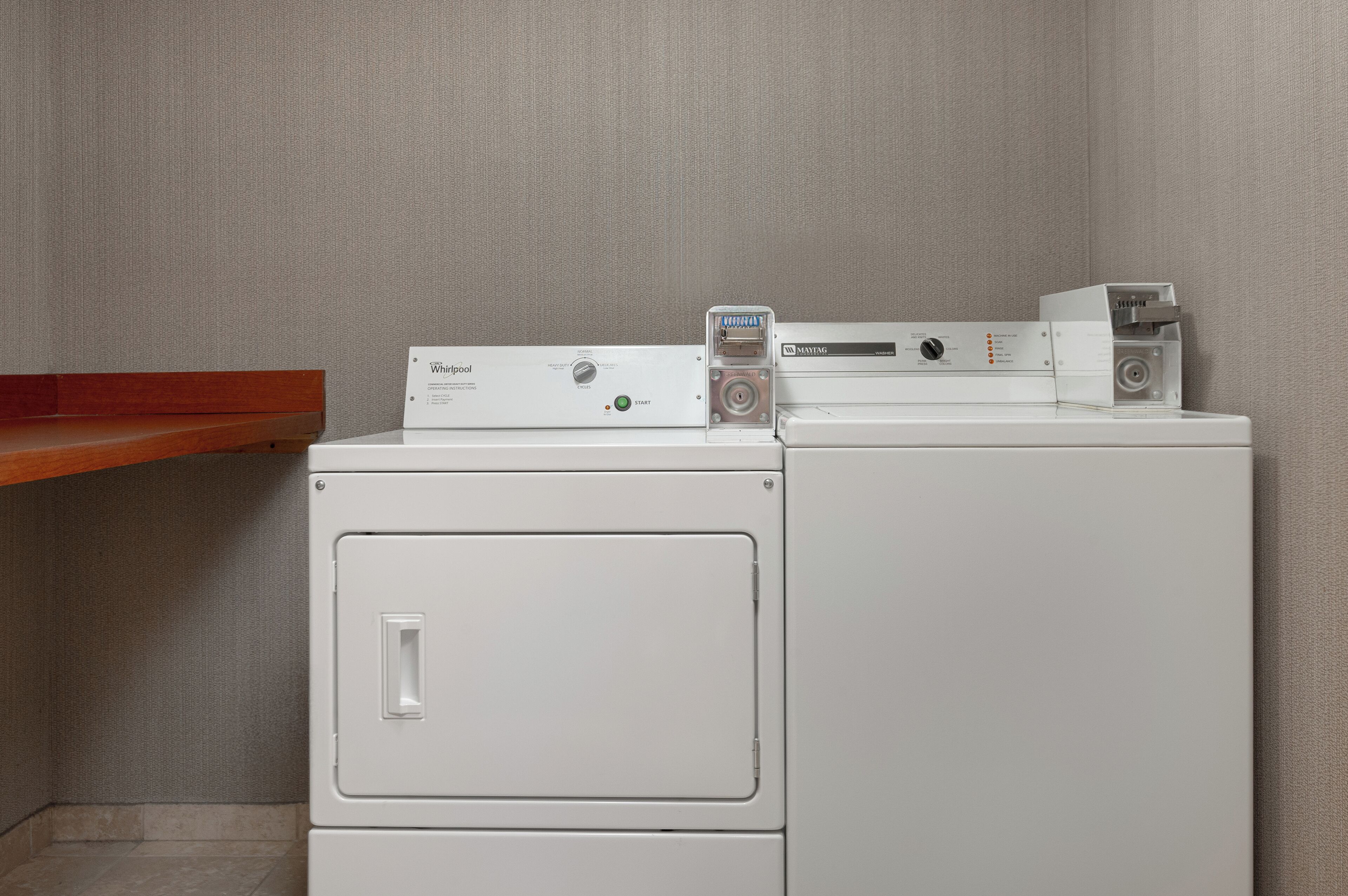 A front-loading washer and dryer stacked on top of each other with a wooden shelf above.