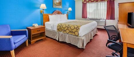 Une chambre d’hôtel comprenant un lit, un bureau, une chaise, une table de chevet, une lampe, un téléviseur et une fenêtre avec des rideaux.